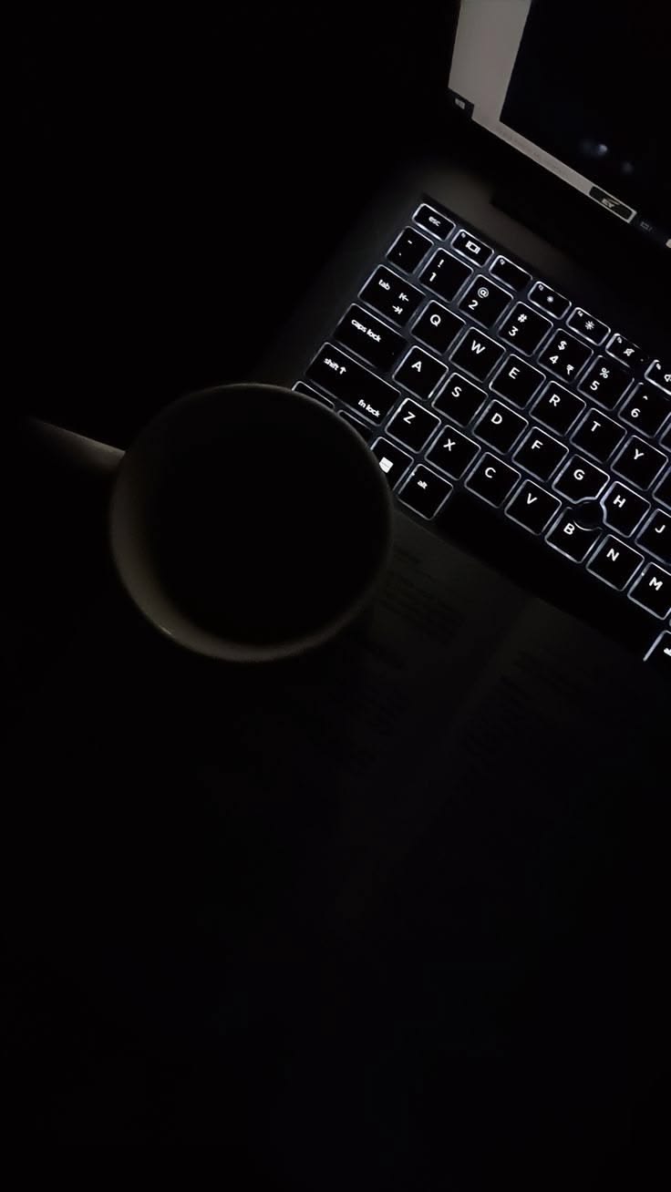 Teclado retroiluminado no escuro ao lado de uma xícara, o trabalho que acontece nos bastidores